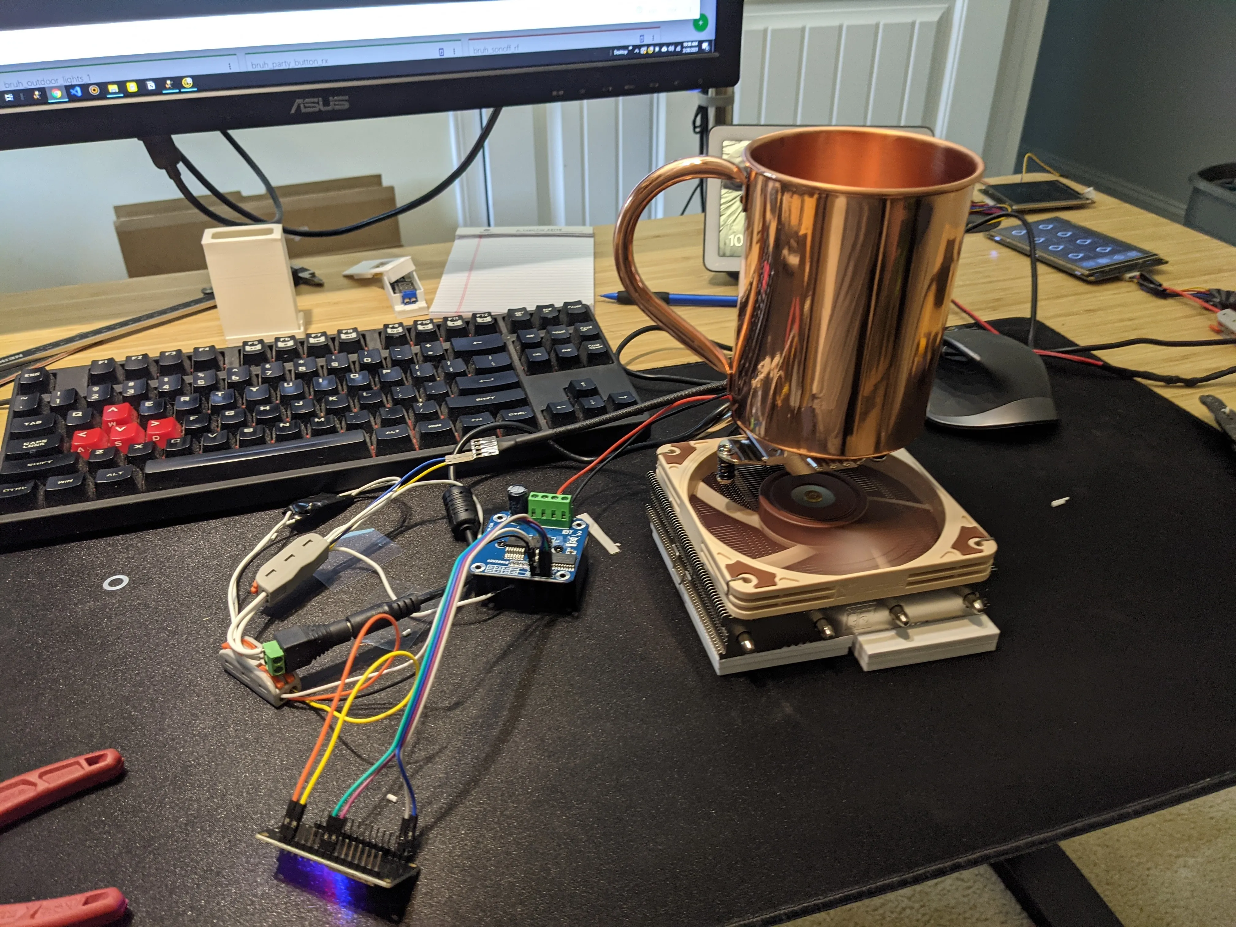 The prototype Peltier bottle warmer on the bench: a copper mug standing on a Noctua low-profile CPU cooler that is clamped to a printed base, with the H-bridge module and dev board wired up alongside